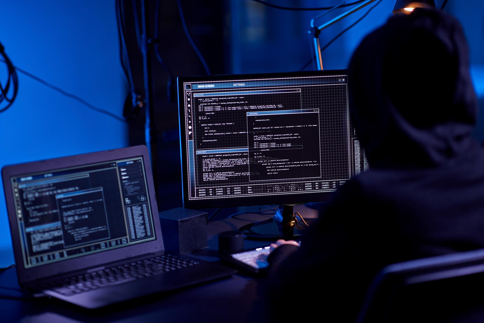 Person coding on multiple screens in a dark room, demonstrating DevOps skills for graduates in 2025.