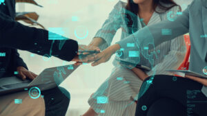 Team members stack hands with digital data graphics overlay, symbolizing tech collaboration.
