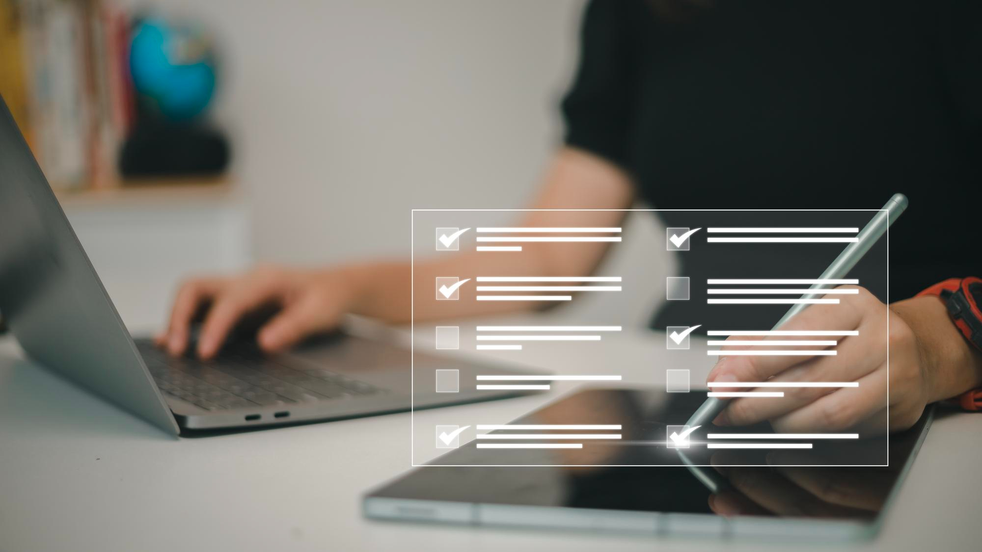 Person completing a digital checklist on a tablet with a laptop beside it.