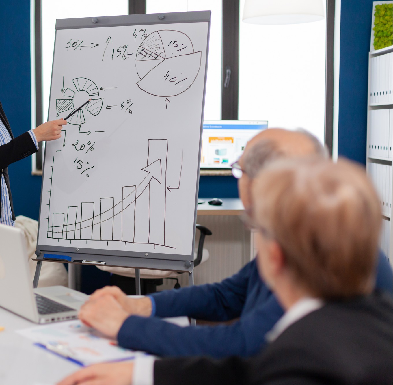 A professional presentation environment where a team is analyzing complex percentages and operational flowcharts on a whiteboard during an infrastructure strategy meeting.